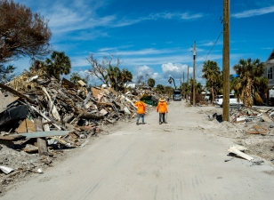 Fort Myers Beach, Florida - October 26, 2022: Workers walking along piles of debris near Estero Blvd