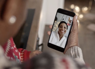 Family members Facetiming, on a video call. One person holds a cell phone, while the other person and a baby are on the phone screen