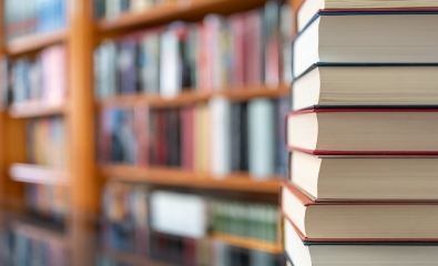 Stack of books in foreground, with many books (blurred) on a shelf in the background