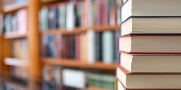 Stack of books in foreground, with many books (blurred) on a shelf in the background