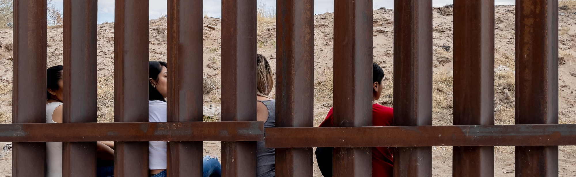 Small group of Mexican people sitting at border wall between Mexico and Texas