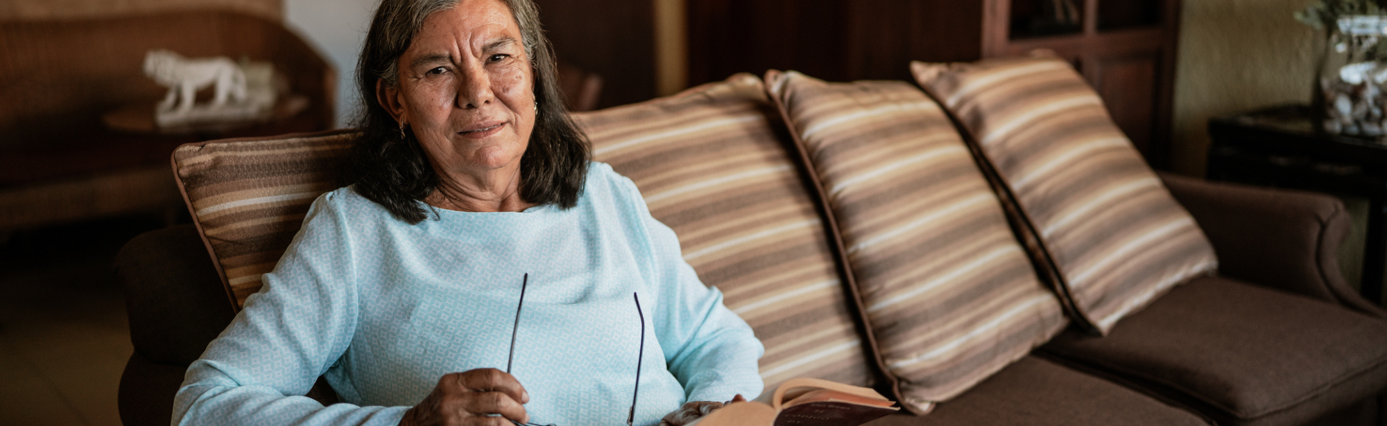 Older woman sitting on couch at home holding eyeglasses