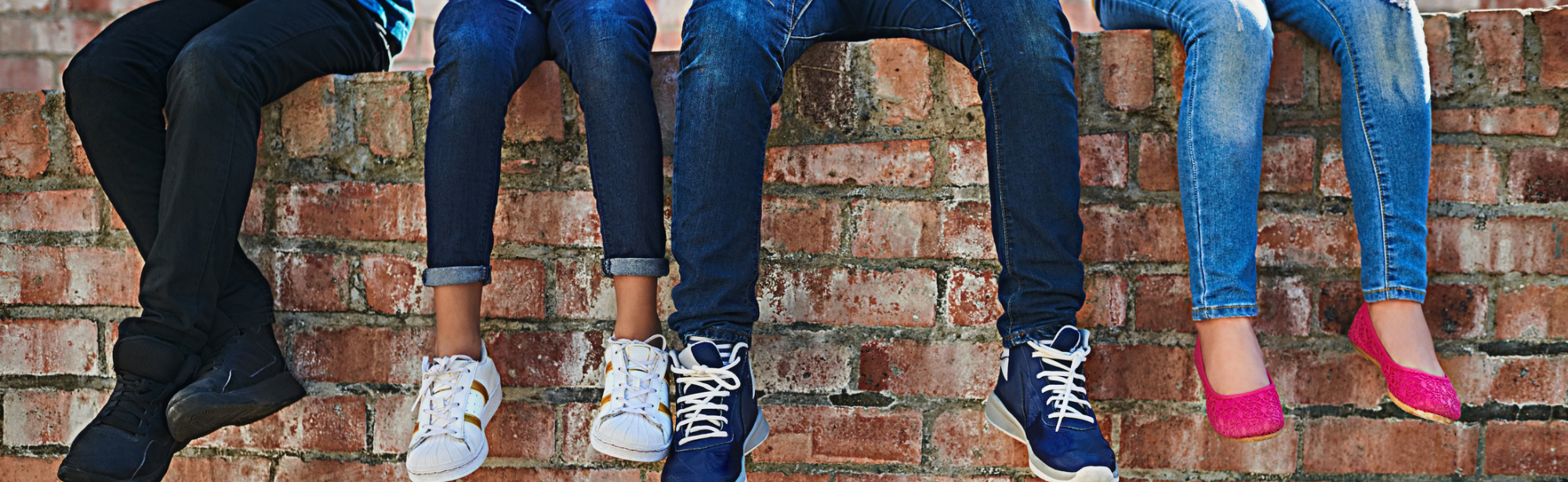 Youth sitting on brick wall, view of their legs and feet