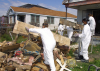 People in white hazmat suits clean up a front yard of a home hit by a disaster
