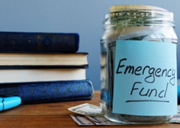 books on table with jar labeled emergency funds with money inside